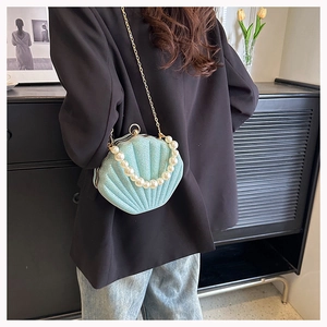 Detail of light blue shell bag with pearl handle and gold chain strap on black blazer