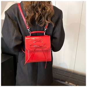Detail of red backpack with bow and crisscross straps on a model in a black suit