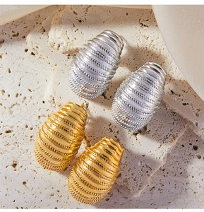 Macro detail of geometric textured gold and silver C-shaped earrings on stone surface