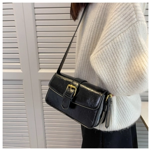 Detail of a black glossy wrinkled shoulder bag with vintage gold buckle closure