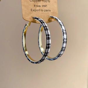 Détail de boucles d'oreilles créoles dorées avec revêtement en tissu pied-de-poule noir et blanc