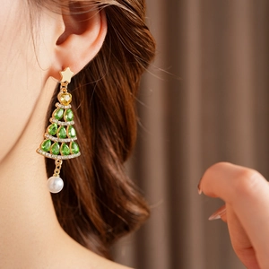 Close-up of golden Christmas tree earrings with green stones and white pearl drops