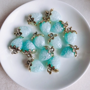 Macro shot of light blue matte strawberry pendants with gold leaf detail in a ceramic bowl