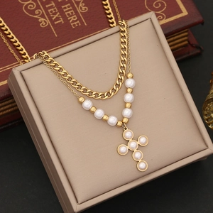 Macro detail of double-layered gold chain with pearl cross pendant and flat link necklace