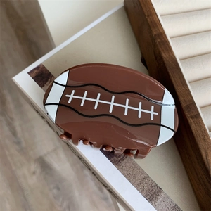 Détail d'une pince à cheveux en acrylique en forme de rugby marron sur un livre