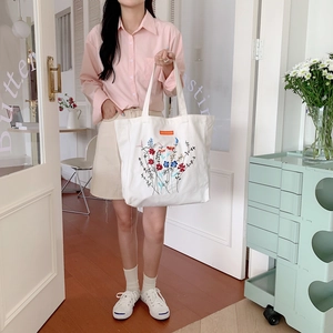 Close-up of vibrant floral embroidery on a cream white canvas tote bag with side tag