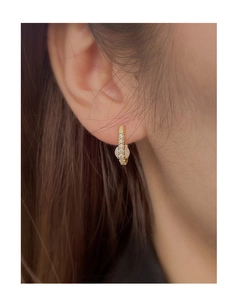 Close-up of golden oval hoop earrings with sparkling zircon and pearl on a model