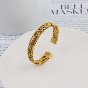 Detailed view of golden twisted mesh open cuff bracelet on a minimalist white stand