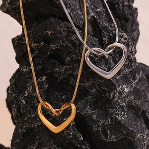 Close-up of gold and silver heart pendants on snake chains over black volcanic rock