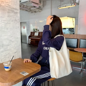 Close-up of white canvas tote bag with navy blue tracksuit set in a cozy cafe setting