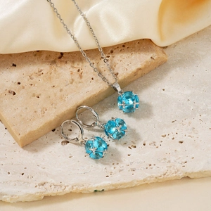 Silver jewelry set with round blue gems on beige stone and champagne satin background