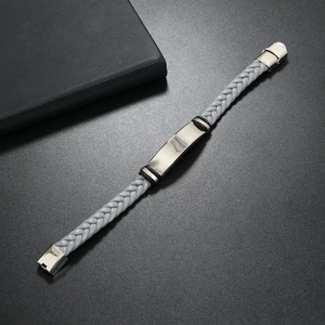 Macro detail of a grey braided leather bracelet with silver metal plate on black background