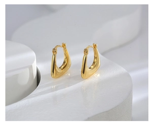 Macro detail of minimalist gold U-shaped earrings on a white geometric display tray