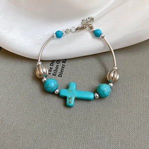 Close-up of turquoise beads bracelet with silver cross pendant on silk background