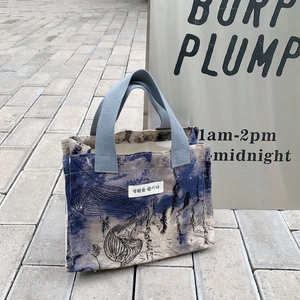 Macro view of portable canvas lunch bag with blue tie-dye print and grey woven handles