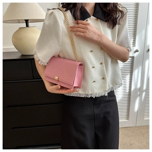 Detail of pink quilted crossbody bag with metal buckle and gold chain strap on model