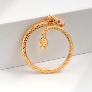 Golden dragon ring with intricate scales and a red gemstone eye on a white base