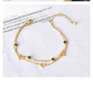 Detail of double-layer gold bracelet with hollow heart and green star charm on book