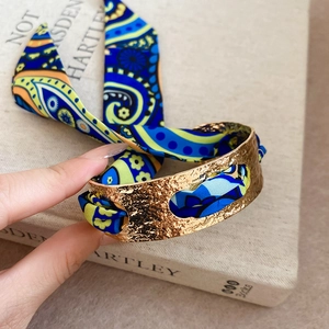 Close-up of bohemian silk scarf wrapped golden cuff bracelet with paisley pattern texture