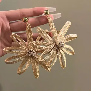 Macro detail of handmade woven sunflower earrings with natural fiber petals and gold studs