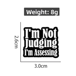 Pin's en émail avec citation 'I'm Not Judging I'm Assessing', noir et blanc, 2.6x3.0cm