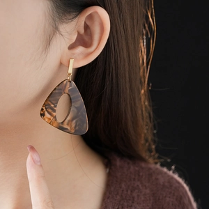 Close-up of a model wearing brown marble leopard resin triangle earrings with gold studs