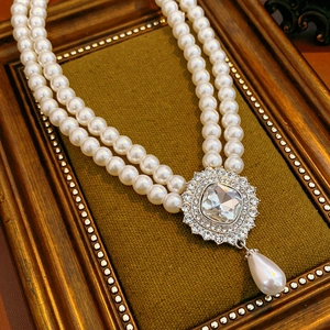 Close-up of double-layer pearl necklace with square crystal pendant on green velvet