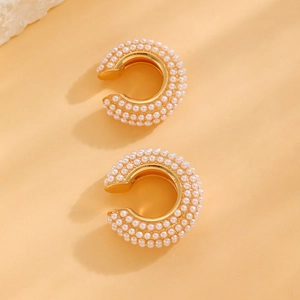 Detailed view of gold C-shaped ear cuffs with multi-row white pearls on pink background