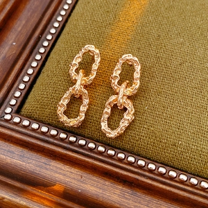 Gros plan de boucles d'oreilles chaîne dorées texturées sur tissu vert foncé vintage