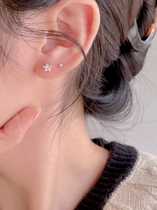 Detail showing small silver 5-petal flower and tiny ball stud earrings worn on ear