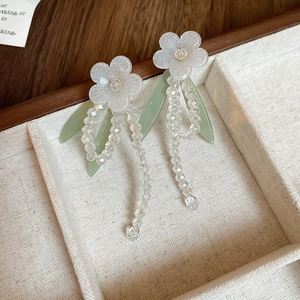 Detail of flower earrings with white petals, green leaves and long crystal tassels