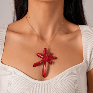 Detail of red flower pendant with gold chain worn over a white knitted sweater