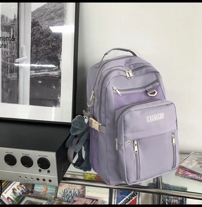 Dettaglio dello zaino in nylon viola con scomparti multipli a cerniera e tasche laterali