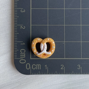 Detailed view of heart-shaped pretzel resin charm with colorful beads on a ruler grid