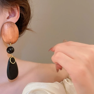 Close-up of long drop earrings with wooden discs and black beads on a model