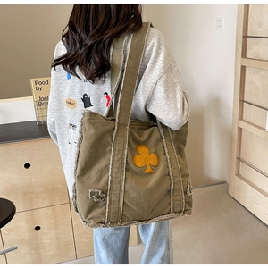 Detail of army green canvas tote bag featuring raw edges and a yellow floral patch
