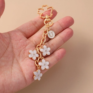 Close-up of golden keychain with white daisy pendants and a round letter U charm