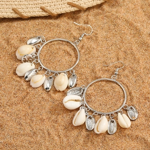 Natural seashell and silver metal hoop earrings on a sandy beach with a straw hat