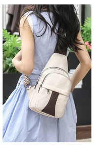 Outdoor shot of a beige canvas chest bag with brown leather trim and geometric strap