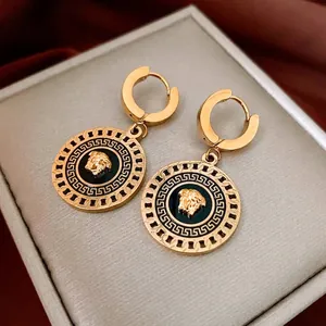 Golden Medusa round hoop earrings with Greek key pattern on red velvet display