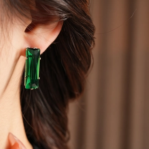 Close-up of elegant emerald green rectangular zircon earrings on a golden setting