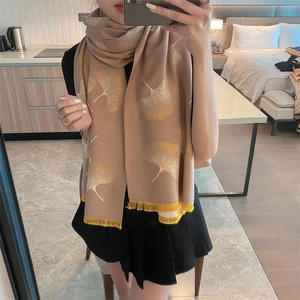Detail of soft beige cashmere scarf with yellow ginkgo leaf pattern and fringe edges