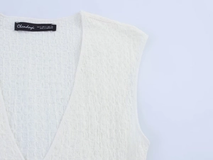 Detail of the white textured knit V-neck top with brand label and fine pleated fabric finish