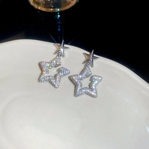 Macro shot of silver star earrings with zircons on white ceramic plate, luxury jewelry detail