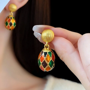 Close-up of vintage golden oval earrings with colorful enamel drop on model's ear
