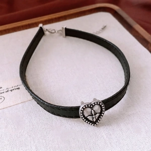 Vintage heart leather choker necklace with silver embossed cross pendant on white fabric
