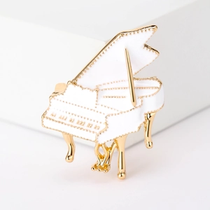 Macro view of white enamel piano brooch with gold metal details on a clean white pedestal
