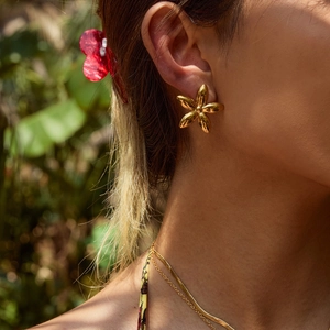 Close-up of a gold floral stud earring worn on ear with natural outdoor background