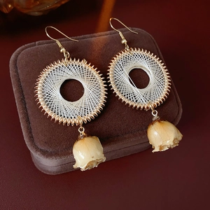 Detail of woven round earrings with gold metal frame and dried rosebud pendant drop