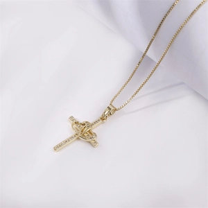 Collana a croce dorata con dettaglio cuore e zirconi su sfondo di tessuto bianco